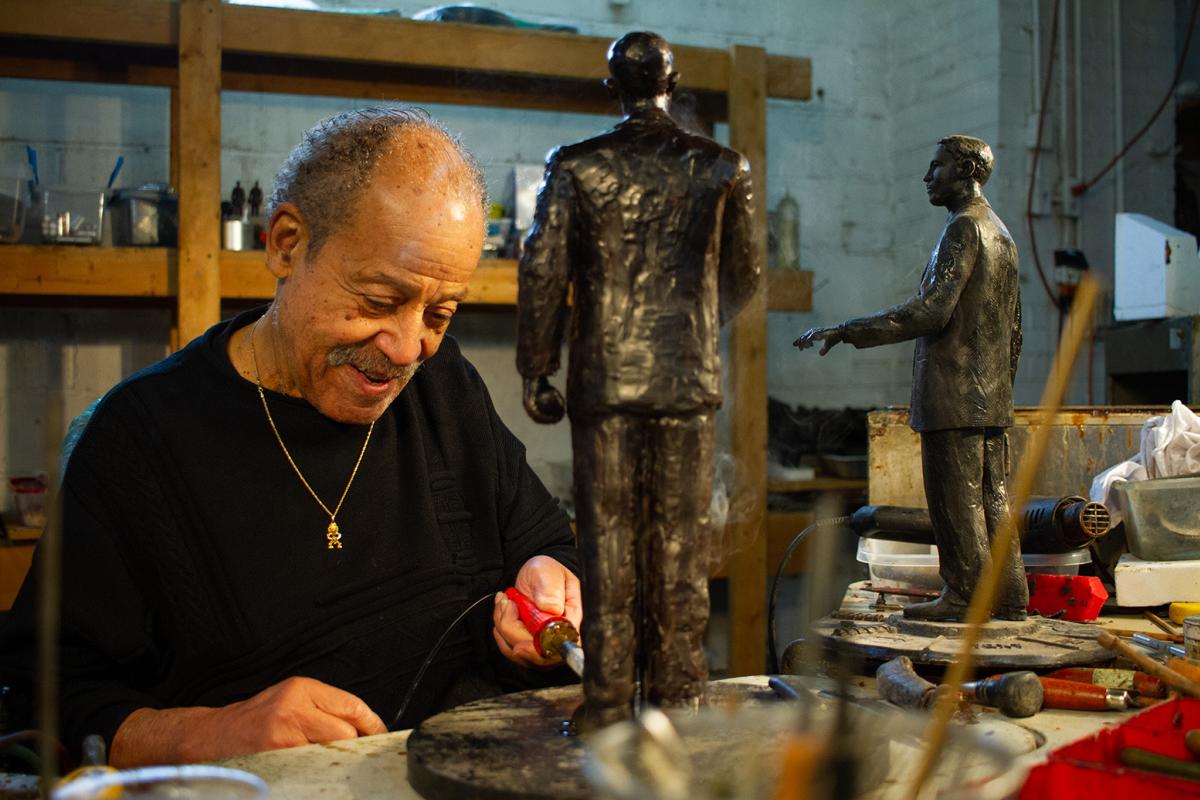 Ed Dwight in his studio, sculpting 2 standing male figures.