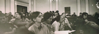 A crowded room of young adults gathered in seats and on the floor.