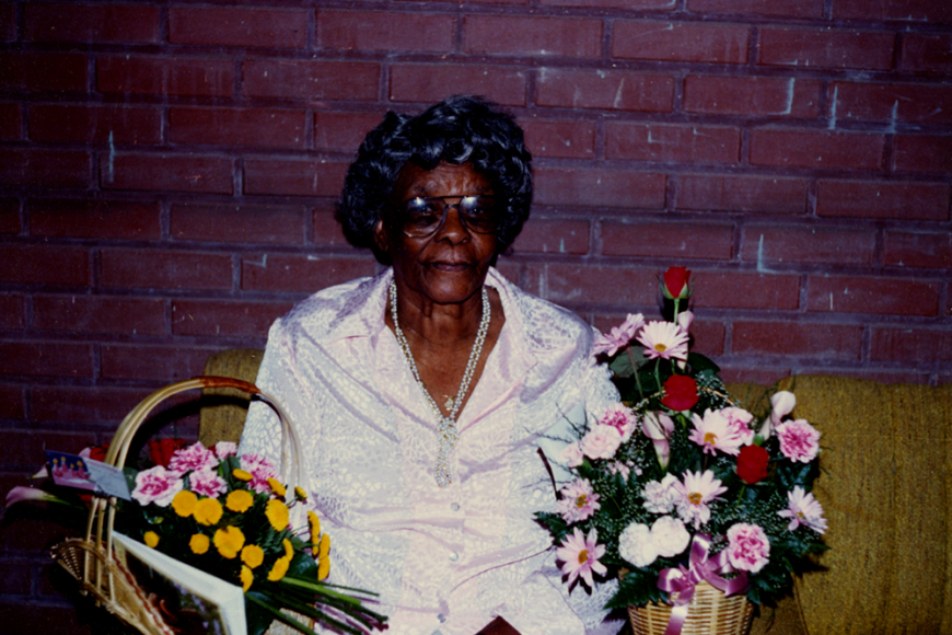Rolan Craig sitting in front of a brick wall surrounded by baskets of pink flowers.