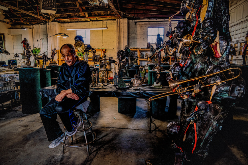 Ed Dwight in his studio surrounded by bronze statues posing with jazz instruments.
