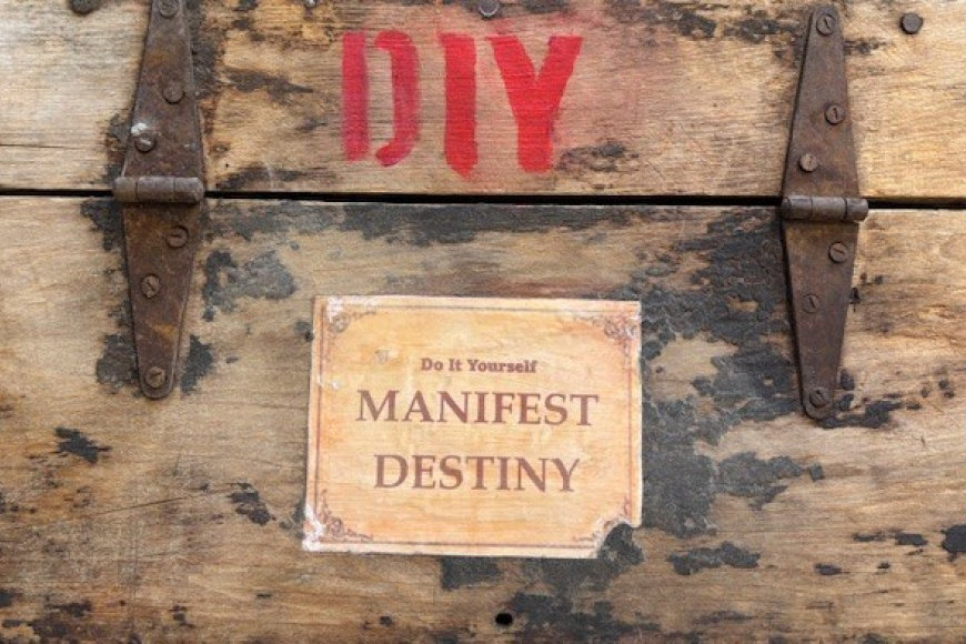 A worn wooden box with stenciled letters reads DIY. In worn paper reads "Do It Yourself Manifest Destiny"