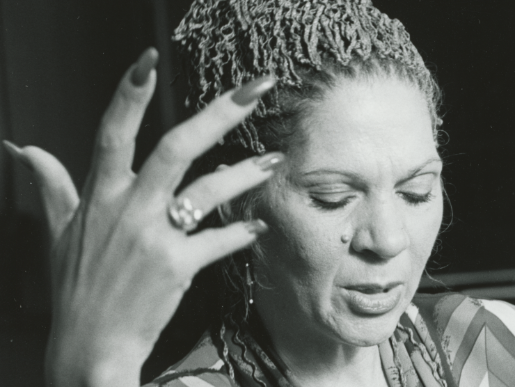 The photograph is a portrait, showing Robinson mid dance with her right hand upright in the air. She is wearing a colorful robe or shirt, and looking down as she moves.