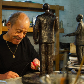 Ed Dwight in his studio, sculpting 2 standing male figures.